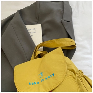 Detail of yellow canvas backpack with blue 'take it easy' embroidery and flap closure