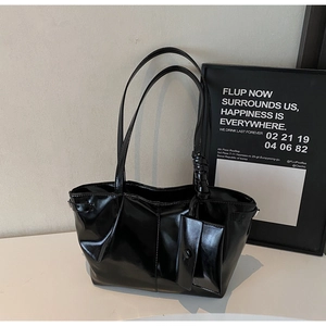 Dettaglio della borsa tote nera lucida con doppi manici e un mini ciondolo a sacchetto
