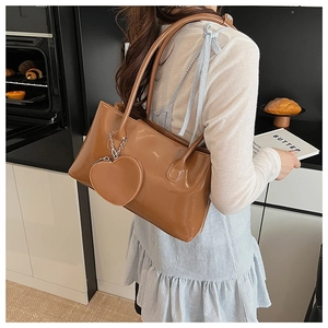 Elegante borsa sottobraccio in vernice marrone con ciondolo a cuore su una modella