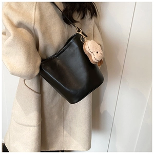 Detail of a black bucket bag with a beige puppy plush keychain and gold hardware