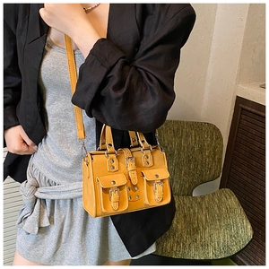 Detail of yellow crossbody bag featuring front buckle pockets and metallic studs