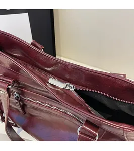 Macro detail of wine red tote bag showing silver metal zipper and glossy leather texture