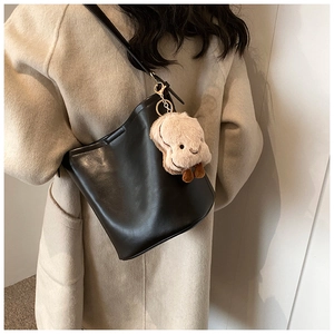Detail view of black leather bucket bag with a cute plush toast charm and gold metal rings