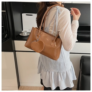 Dettaglio borsa tote in pelle verniciata marrone con ciondolo a cuore su modella
