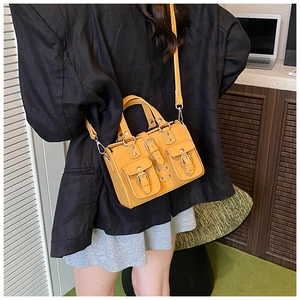 Detail view of mustard yellow leather crossbody bag with metal rivets and buckle pockets