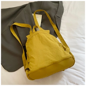 Detail of mustard yellow nylon backpack with drawstring pockets on white fabric and suit