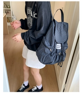 Detail of checkered drawstring backpack featuring a side zipper pocket and woven straps