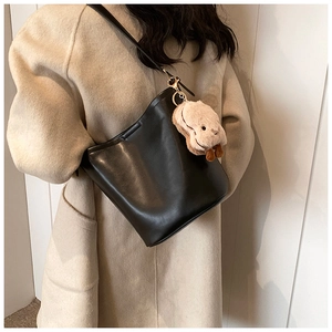 Detail of matte black bucket bag featuring golden hardware and a plush puppy charm