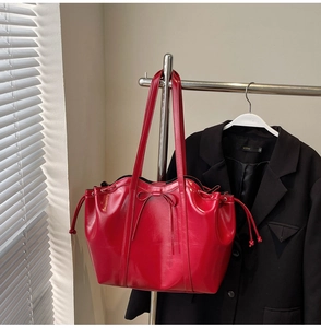 Close-up of red patent leather tote bag featuring a bow decoration and drawstring side detail