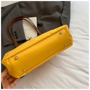 Detail of yellow tote bag base with four silver metal feet and neat stitching on leather