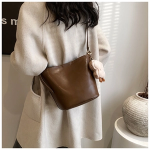 Detail of dark brown leather bucket bag with plush charm on a beige coat model