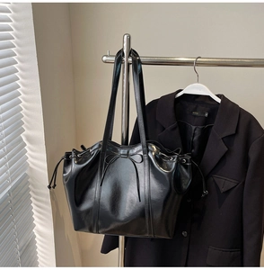 Detail of black glossy leather tote bag with drawstring and decorative bow on a rack