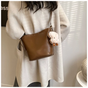 Chic brown leather bucket bag with white cloud plush charm worn over a beige coat