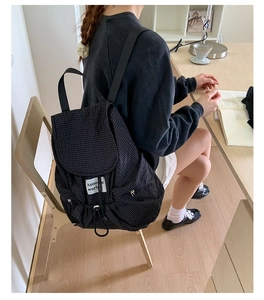 Close-up of black plaid pattern backpack featuring a white logo tag and drawstring closure