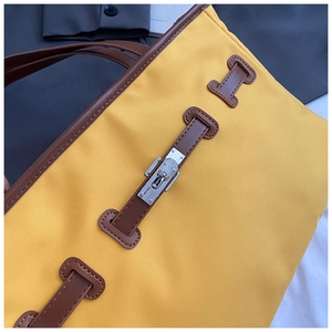 Detail of yellow nylon tote showing silver turn-lock and brown leather strap textures