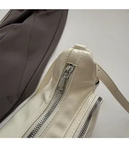 Close-up of smooth silver metal zipper and stitching on cream PU leather shoulder bag