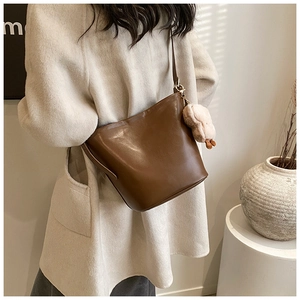 Close-up of a brown bucket bag featuring a soft plush charm and adjustable shoulder strap