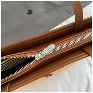 Detailed macro view of the silver zipper and branded puller on the brown bucket bag