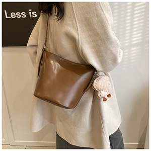 Brown bucket bag side view with white alpaca plush charm on a beige coat outfit
