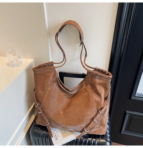 Detail view of large brown vintage tote bag with side buckles on black suitcase
