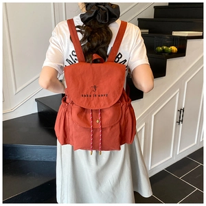 Detail of red-brown canvas backpack with 'take it easy' embroidery and drawstring closure