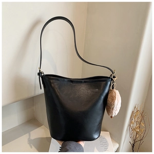Close-up of minimalist black leather bucket bag with a soft plush pendant and shoulder strap