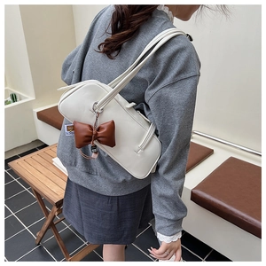 Détail d'un sac baguette en cuir blanc avec pendentif nœud marron porté à l'épaule