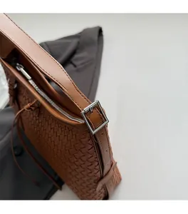Close-up of brown woven leather bag with adjustable silver metal buckle and zip closure