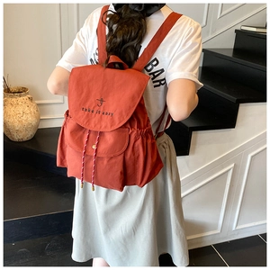 Detail of brick red canvas drawstring backpack with embroidered take it easy text on flap