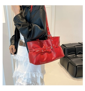 Détail du sac à bandoulière en cuir rouge avec œillets métalliques et texture plissée