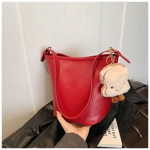 Detail of red leather bucket bag featuring a cute plush animal charm and adjustable strap