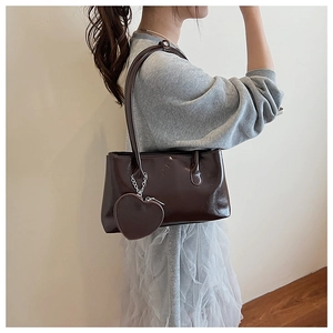 Vista laterale della borsa a spalla in pelle marrone lucida con ciondolo a cuore su modella