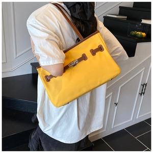 Detail of yellow tote bag with brown leather trim and metallic turn-lock closure
