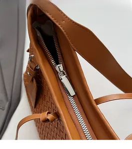 Close-up of silver metal zipper and woven leather texture on a brown shoulder bag