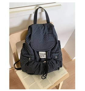 Detail of grey plaid backpack with drawstring closure and front label on a chair