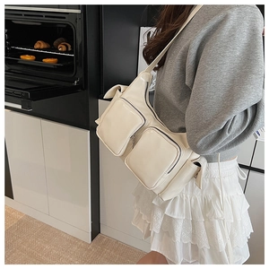 Detail of a retro cream multi-pocket crossbody bag with wide shoulder strap worn by model