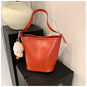 Close-up of caramel PU leather bucket bag with a cute plush puppy charm on a wooden stand