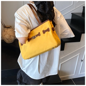 Detail of yellow bucket bag featuring brown leather trim and silver metal twist lock buckle
