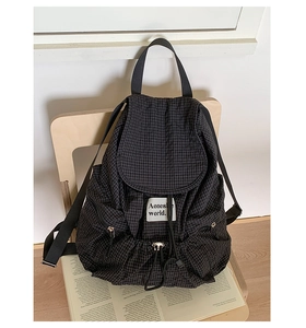 Detail of black plaid drawstring backpack with Aonesworld label resting on a wooden chair