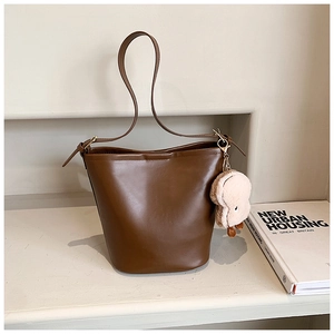 Detail of dark brown bucket bag featuring a soft faux leather finish and plush pendant