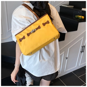 Detail of yellow canvas bucket bag showing brown leather trim and metal lock closure