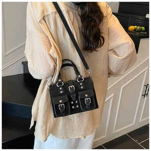 Detail of black multi-pocket handbag with silver rivets and buckles on a model