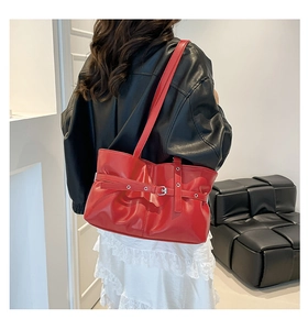 Détail d'un sac à bandoulière rouge brillant avec boucle décorative et plis en cuir chic