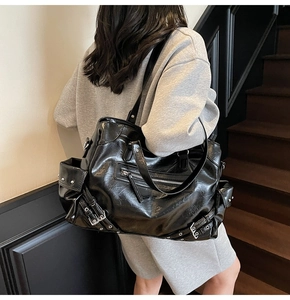 Detail of black punk tote bag with metallic studs, zippers and buckles on a female model