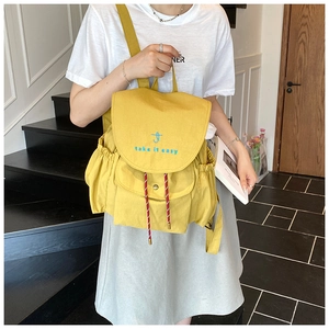 Close-up of yellow canvas backpack with blue embroidery and decorative red drawstring