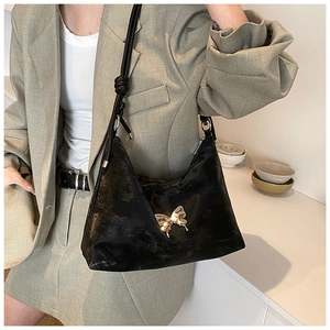 Close-up of black shoulder bag featuring gold butterfly buckle and knotted leather strap