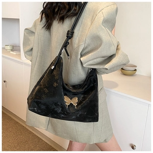 Detail of black tote bag featuring metallic butterfly buckle and knotted shoulder strap