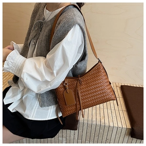Detail of a brown woven leather shoulder bag with matching tassel and slim strap