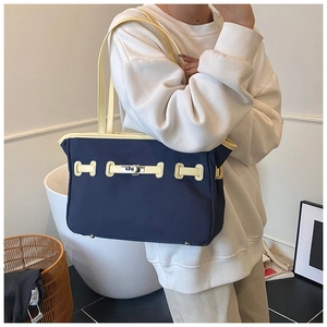 Detail of navy contrast tote bag featuring silver turn-lock and beige handles in home setting