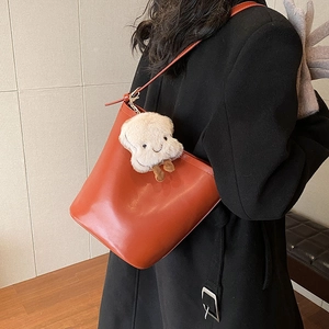 Brown leather bucket bag with cute plush pendant shown on model for a trendy casual style